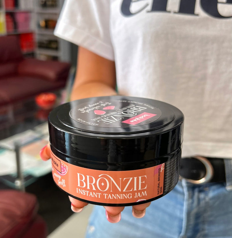 Bodybite BRONZIE Instant Tanning Jam with Watermelon and Mango in a black jar held by a person