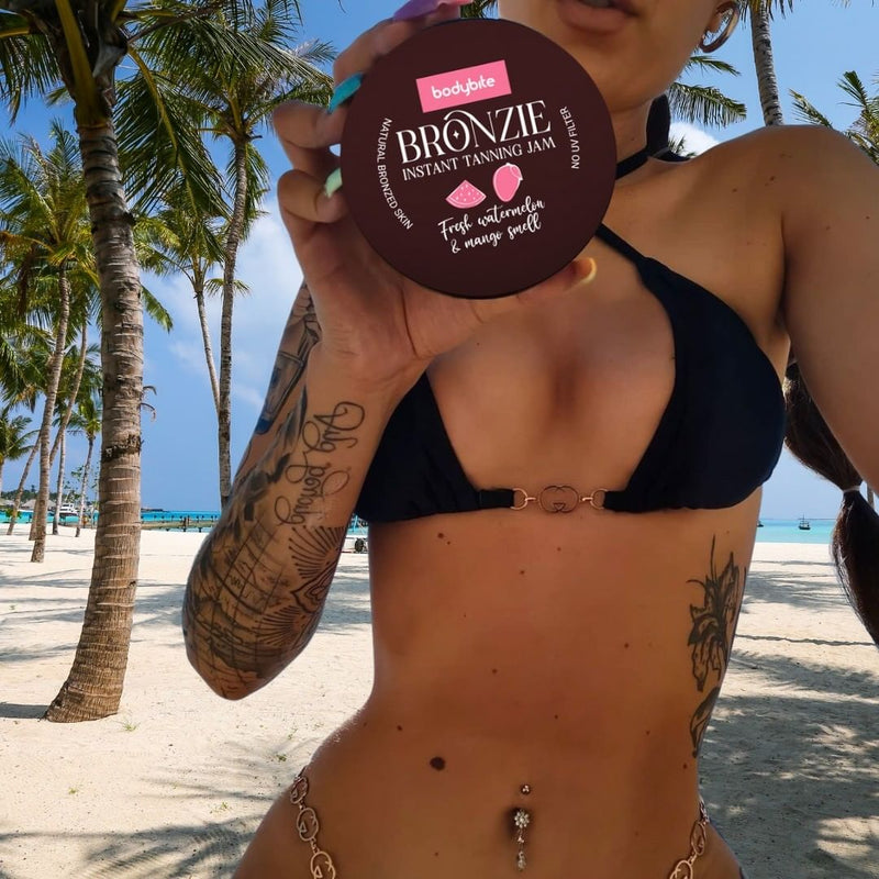 Bodybite BRONZIE Instant Tanning Jam with Watermelon and Mango held by a woman in a bikini on a beach